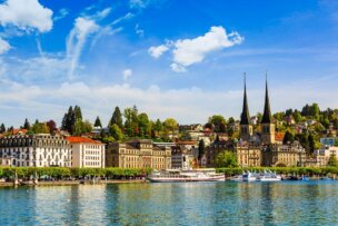 Discover the scenic view of Lucerne, Switzerland, as highlighted in many travel guides. Marvel at its historic buildings, shimmering lake, and distant hills under a partly cloudy sky—a picturesque setting teeming with things to do.