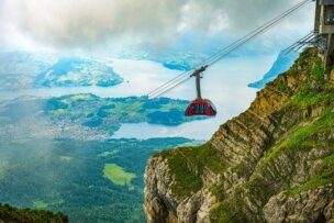 A red cable car ascends along a steep mountain in Lucerne, offering stunning views of the lake and patchwork landscape below under a partly cloudy sky—truly one of the top travel activities to experience among the various things to do.