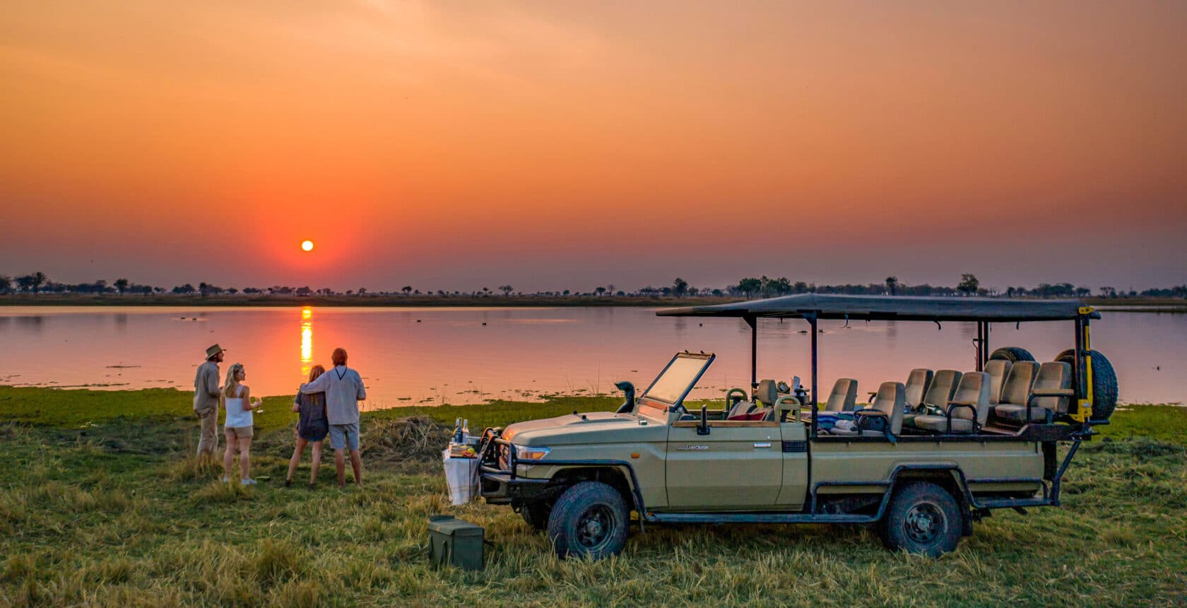 A group of travelers watching a sunset on a safari in Moremi National Park in Botswana.