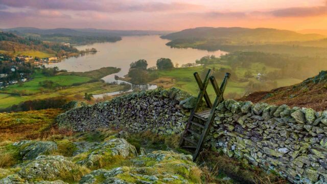 Beautiful sunset over Windermere in the Lake District with a stile and stone wall in the foreground.