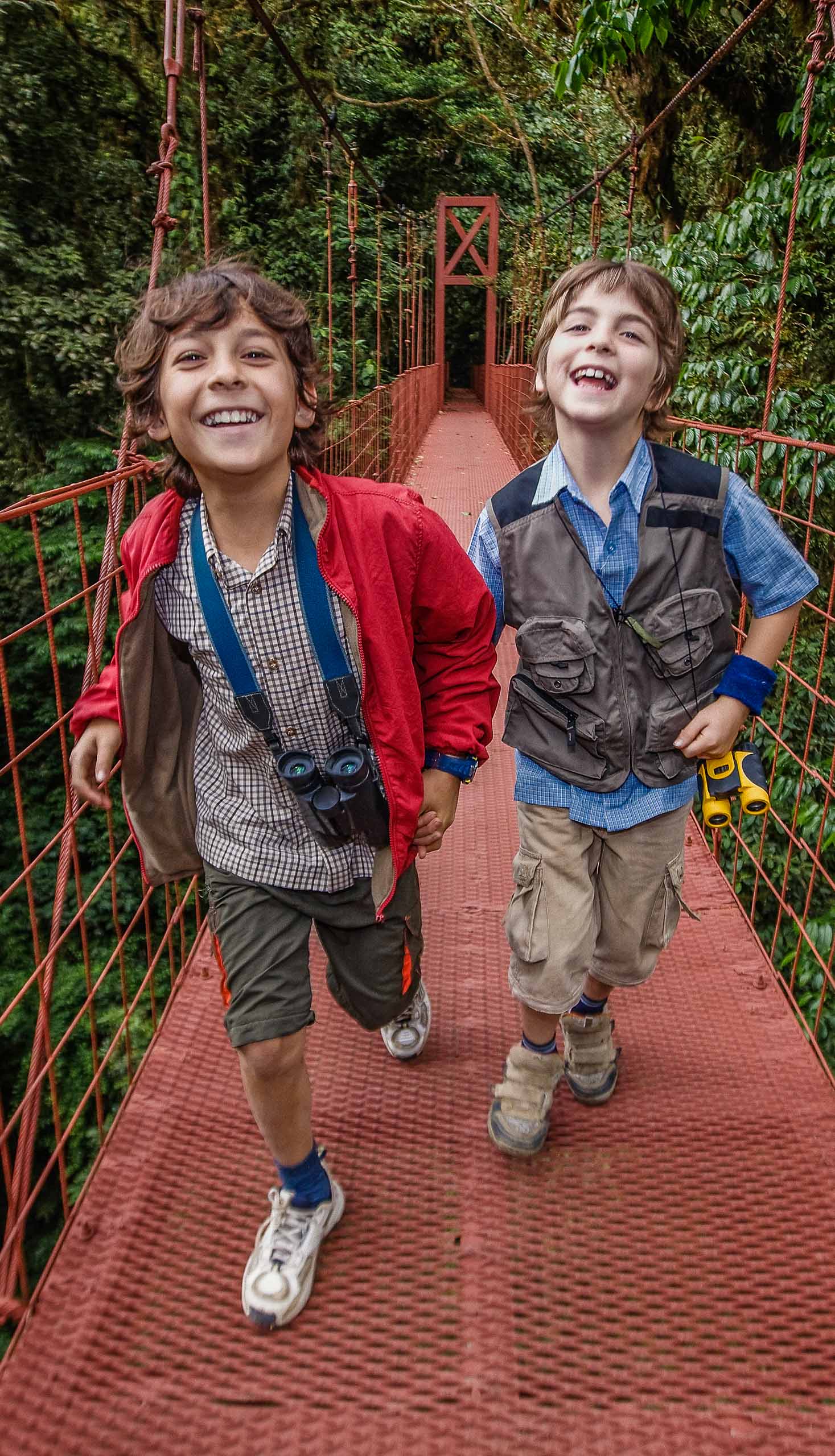 Young boys running across hanging bridge in a rainforest in Costa Rica.