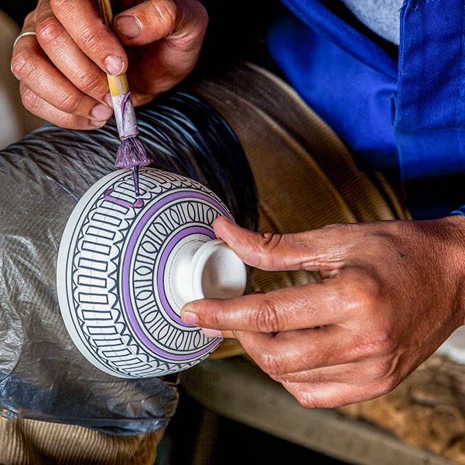 Close-up of an artist's hands as he paints a Moroccan ceramic bowl with geometric patterns.