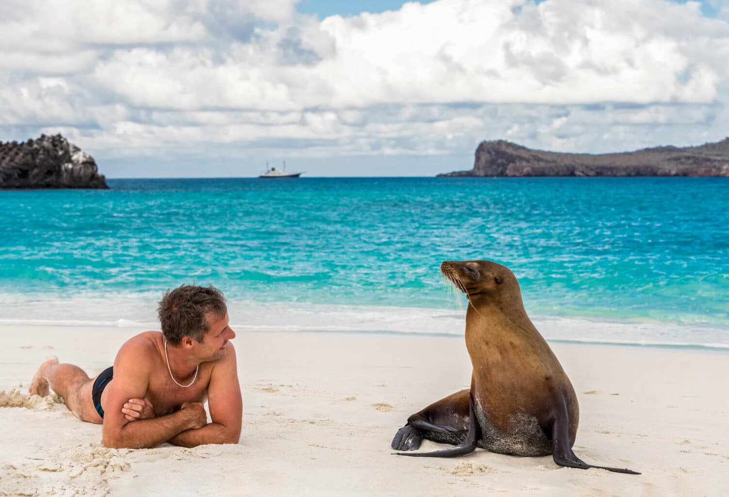 A man alongside a sea lion on a shore of a beach in the Galapagos Islands.