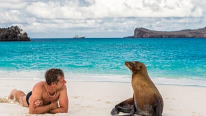A man alongside a sea lion on a shore of a beach in the Galapagos Islands.