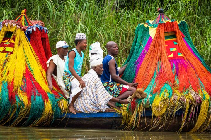 Zangbeto' traditional guardians of the night, and priests in boat going to visit another village.