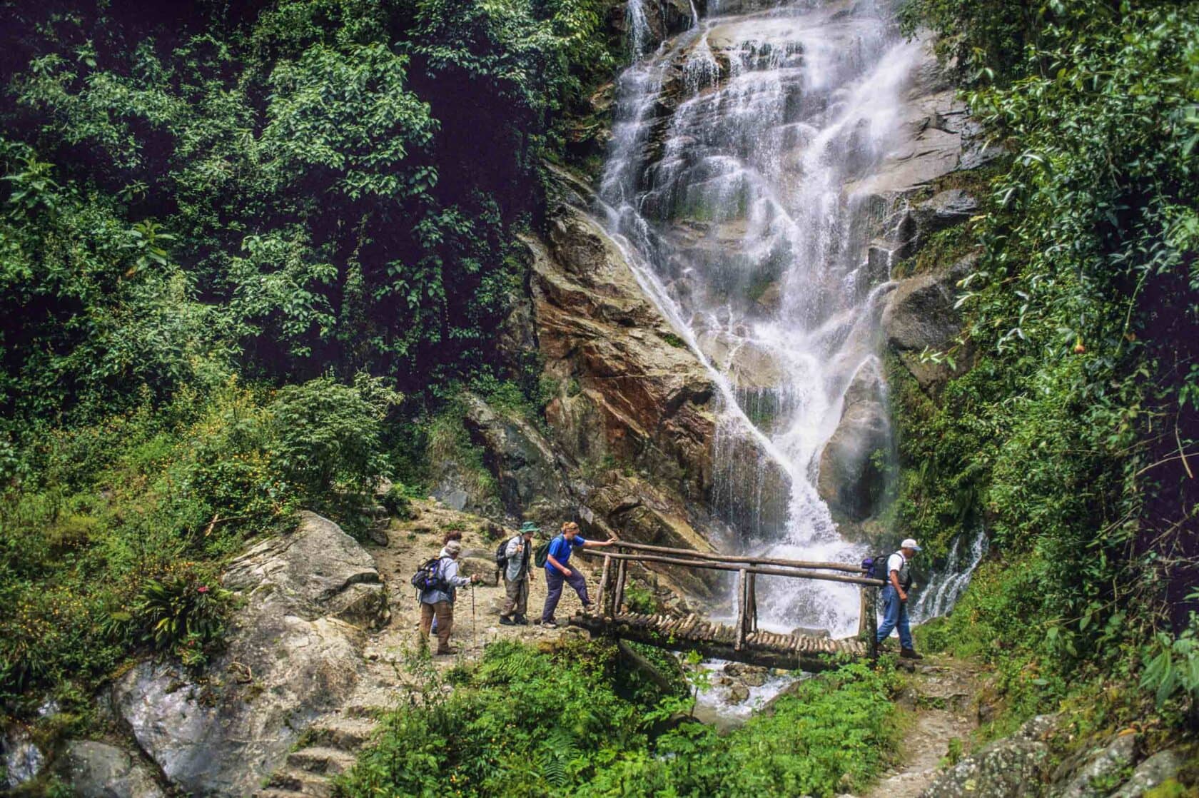 Hikers crossing a stream by the waterfall below Winay Wayna in Peru.