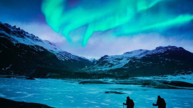 Two travelers hiking by the Northern Lights.