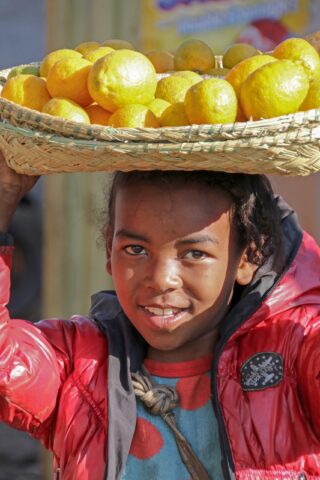 Boy in Madagascar with lemons in basket on head.