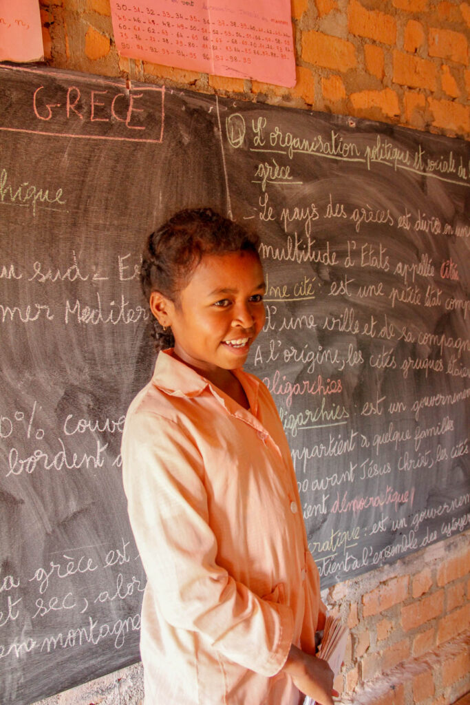 Madagascar schoolgirl stands in front of chalkboard.