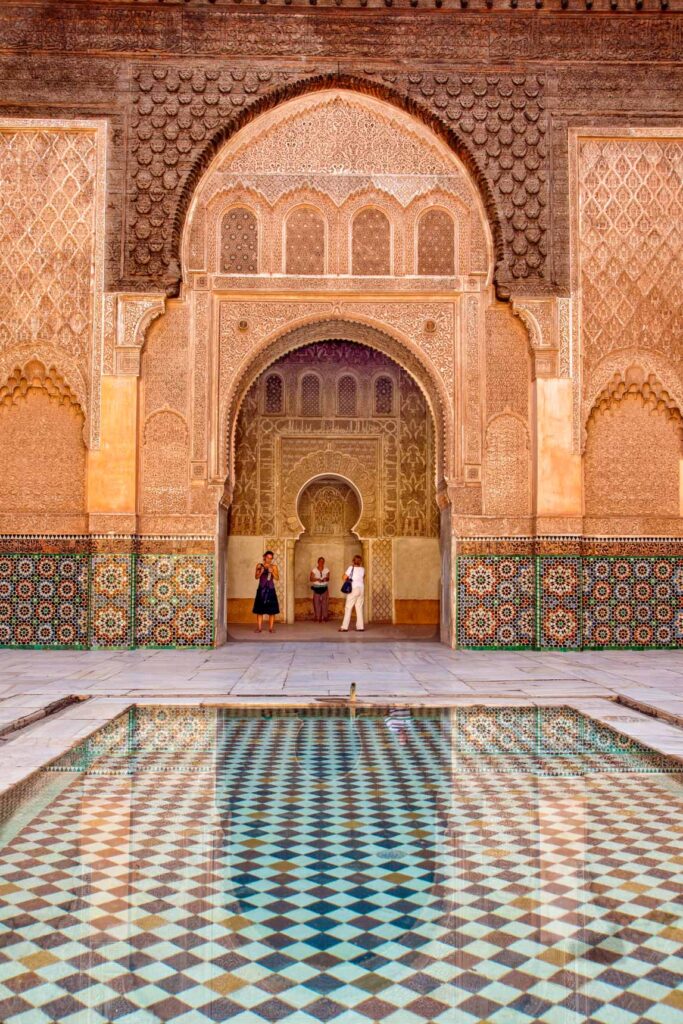 Intricate Moorish architecture with elaborate geometric tilework stands behind a calm reflecting pool.
