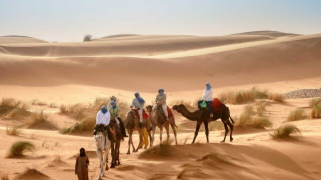 A group of travelers riding camels in a desert in Morocco.