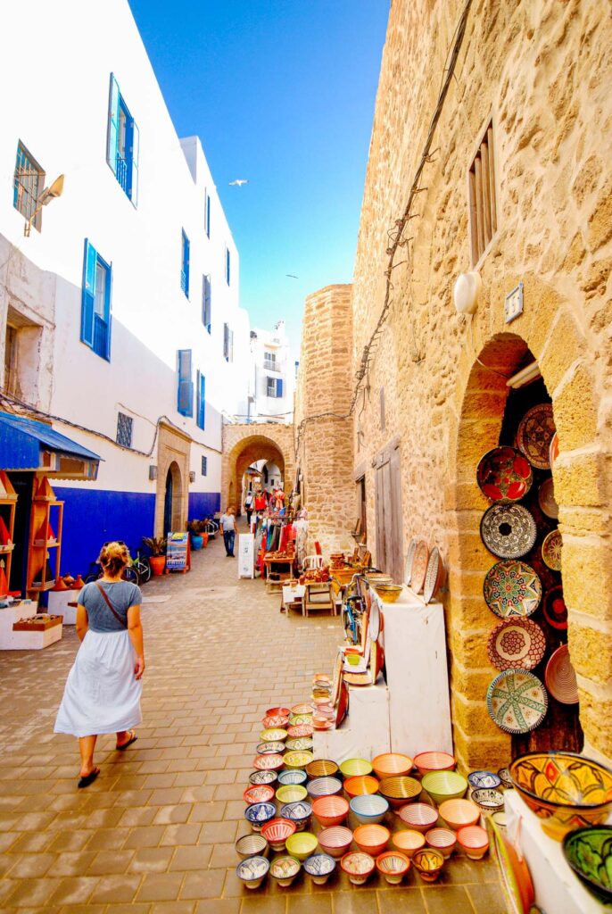 Woman walks down a clean, wide alleyway in a Moroccan medina with colorful ceramics in the foreground.