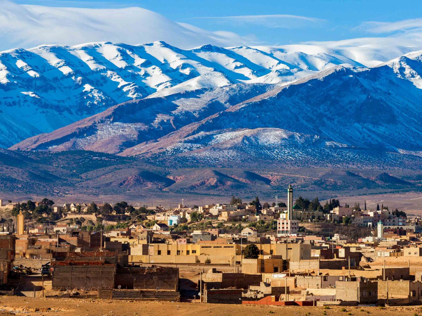 Winter snows cover the High Atlas Mountains in the background with a small town in the foreground.