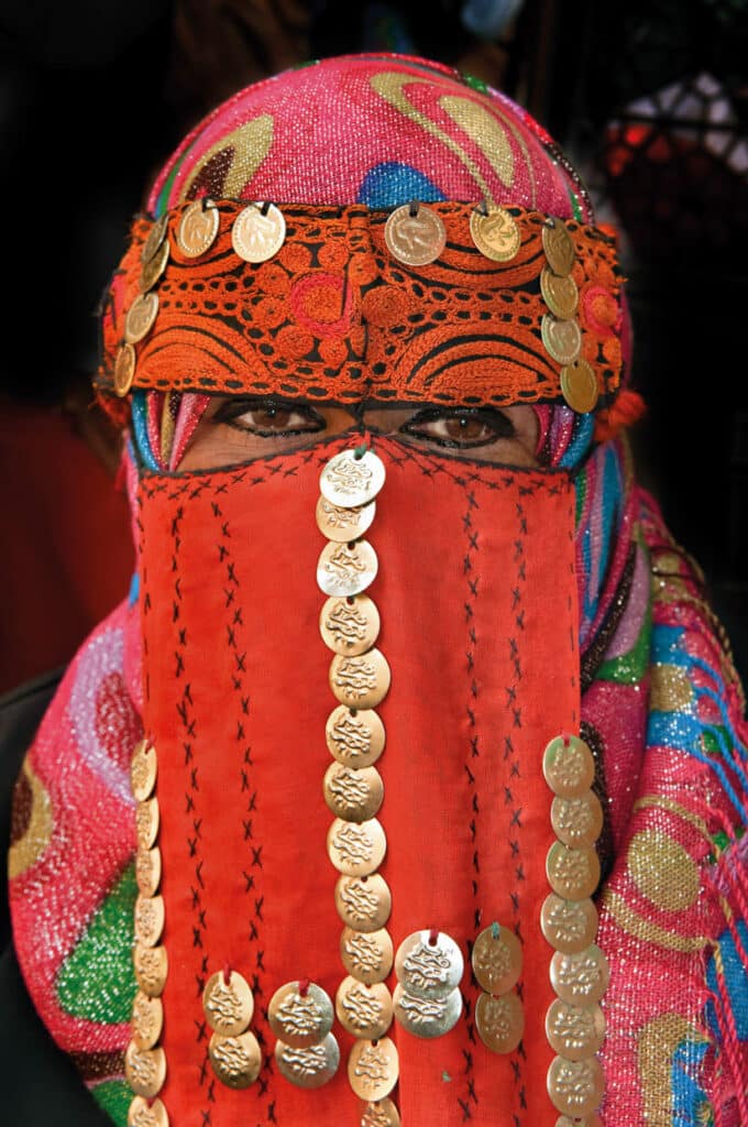 Mysterious Moroccan woman peers out from behind colorful face-covering hijab that is decorated with gold and embroidery.