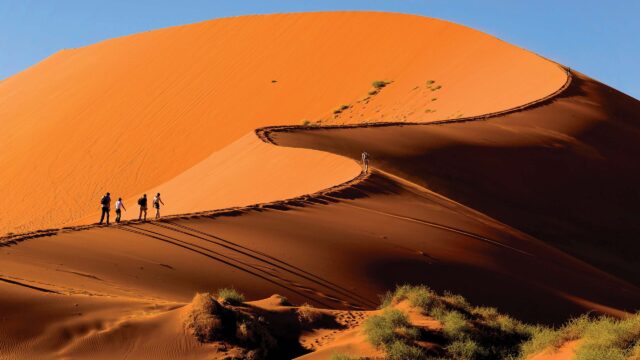 Tourists climbing the red dunes at Sossusvlei, Namibia.