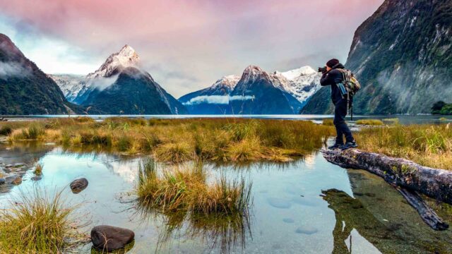 Man photographing sunset at Milford Sound, Fiordland National Park, Southland, New Zealand.