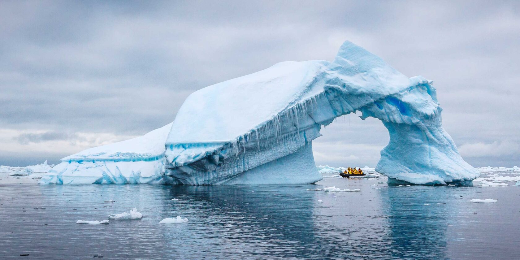 A boat of tourists inspect an iceberg with an arch in Antarctica.