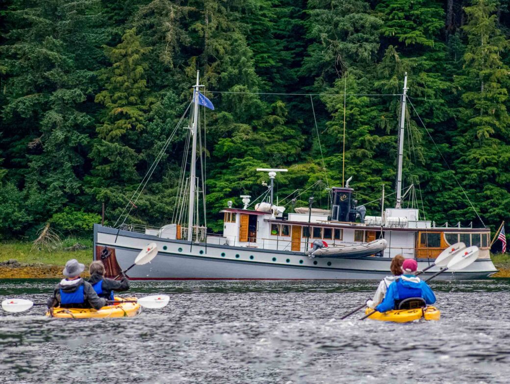 Travelers kayaking in front of a boat in the San Juan Islands.