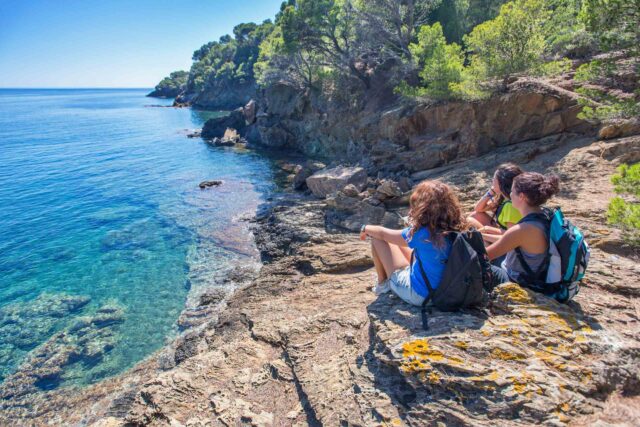 Three hikers taking a break on some rocks overlooking the ocean.