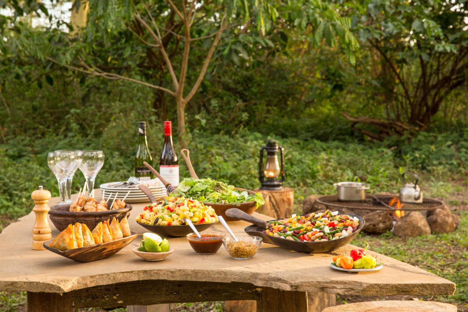 An outdoor dining table set with food and drinks.