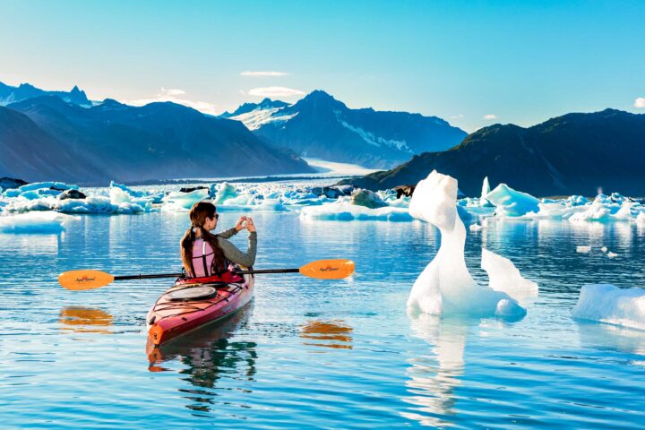 A kayaker taking a photo of an iceberg in Alaska.