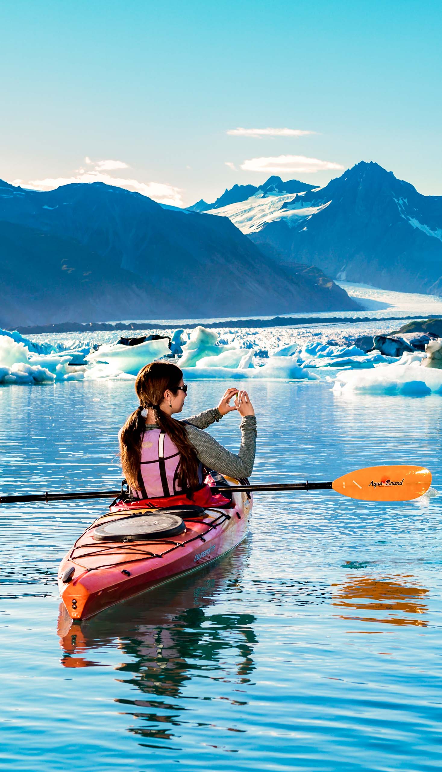 A tourist on a kayak, taking photos of icebergs.