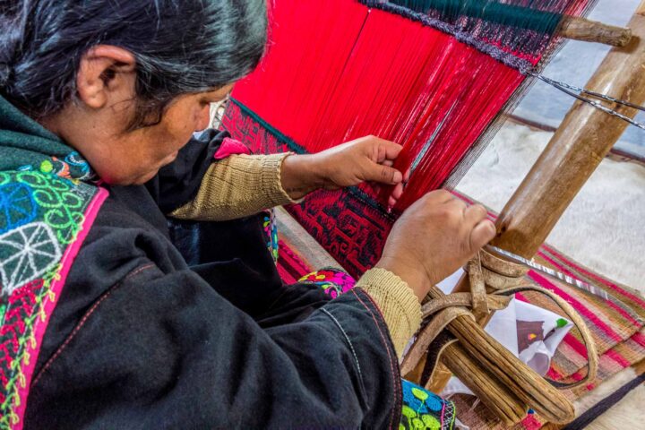 A weaver reaving a red rug.