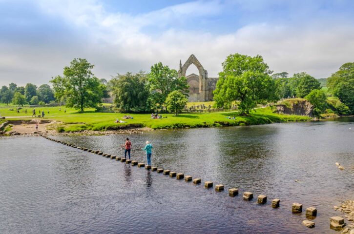 Tourists on the stepping stones across the River Wharfe next to the ruins of Bolton Abbey in the Yorkshire Dales.