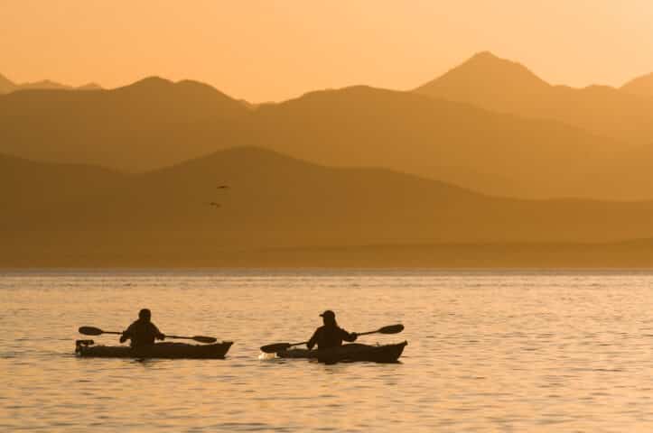Man and woman kayaking in sea at sunset