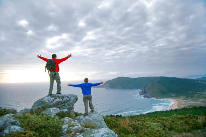 Two hikers on a peak overlooking a beach.