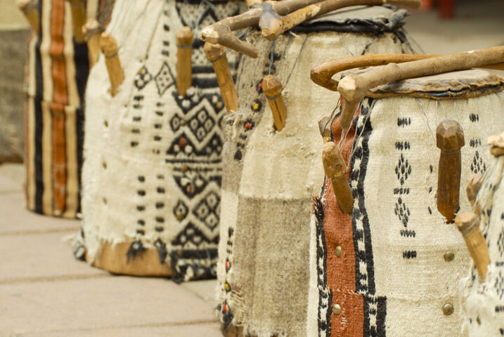 Traditional drums with decorated cloth coverings and wooden handles displayed in an outdoor setting, reminiscent of the instruments that might have been played in the court of an Ashanti King.