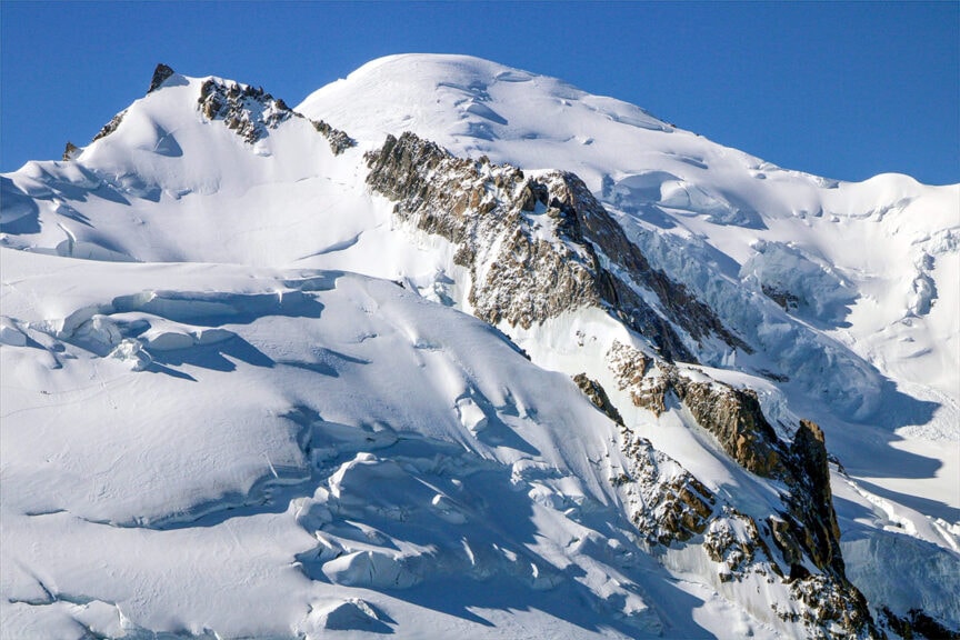 Snow-covered mountain peaks with jagged rocky sections under a clear blue sky, perfect for hiking the iconic Haute Route from France to Switzerland.