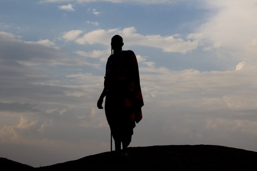 Silhouette of a person exploring a hilltop against a cloudy sky during sunset in East Africa.