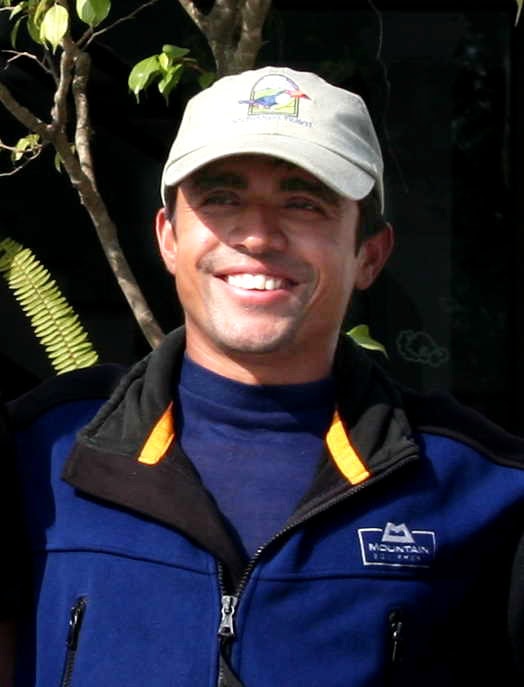 A man wearing a blue zip-up jacket and a beige cap, smiling while posing outdoors for a family photobook.