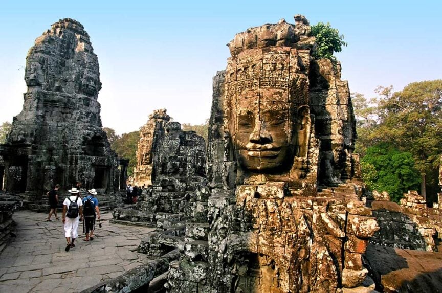 Tourists walk among the ancient stone faces of Bayon Temple in Angkor Thom, Cambodia, as the sunrise casts a golden glow similar to the nearby Angkor Wat.