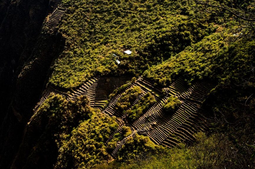 Aerial view of terraced fields on a green hillside at Choquequirao, where shadows highlight the awe-inspiring contours of the terrain.