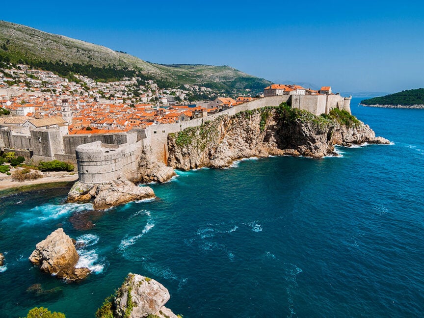 View of Dubrovnik's colorful old town and fortifications on a rocky coastline with clear blue sea on a sunny day, showcasing one of the world's most breathtaking cities.