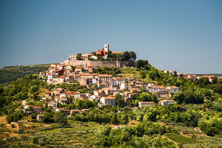 A charming hilltop village with clustered houses and a quaint church, set amidst lush greenery, offers the perfect escape for hiking enthusiasts. Experience the serene beauty of Europe away from the bustling crowds under a clear blue sky.