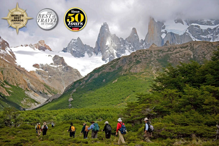 A group of hikers traverse a lush green valley with snow-capped mountains in the background, reminiscent of a Triple Crown adventure. Several award badges are displayed at the top-left corner of the image, showcasing recognition within the travel industry.