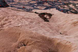 A sea turtle partially buried in sand near fishing nets and boats on a beach with ocean waves and rocky cliffs in the background, reminiscent of the serene coastlines of Oman.
