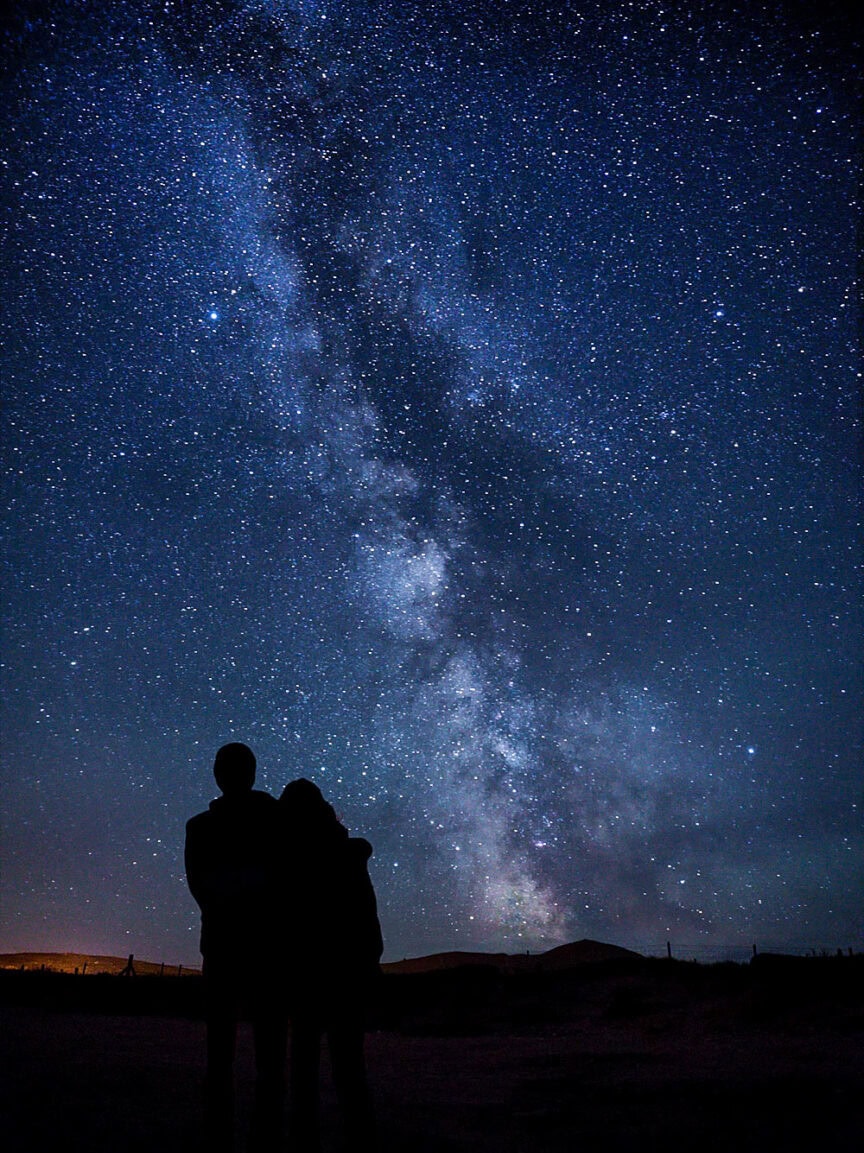 Two people standing close together, silhouetted against a star-filled night sky with the Milky Way visible above—a perfect scene for stargazing and one of the best places to visit.