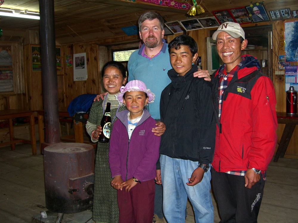 A group of five people, four men and two women, pose together inside a wooden room with a stove, capturing a precious moment for their family photobook in Nepal.