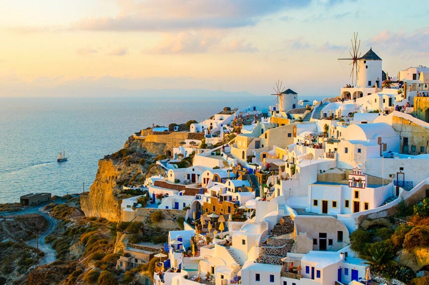 Sunset view of Santorini, Greece, a highlight in colorful cities around the world, featuring white buildings, windmills, and the Aegean Sea in the background.