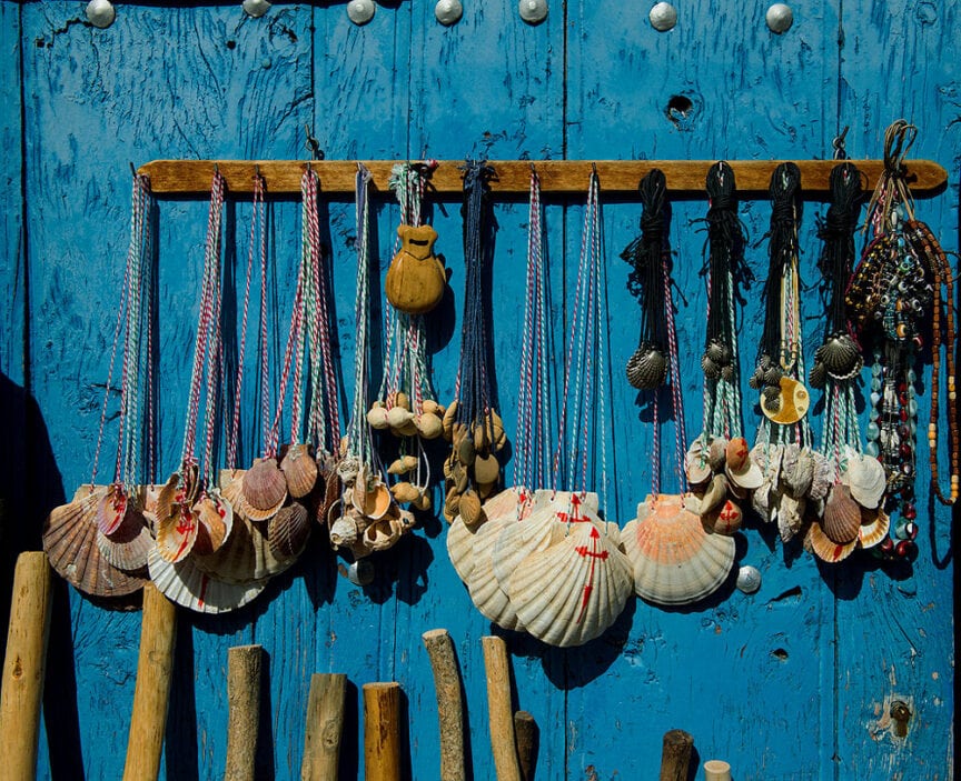 Various shells and small items hanging on strings, displayed on a blue wooden wall, evoke the spirit of "Buen Camino.