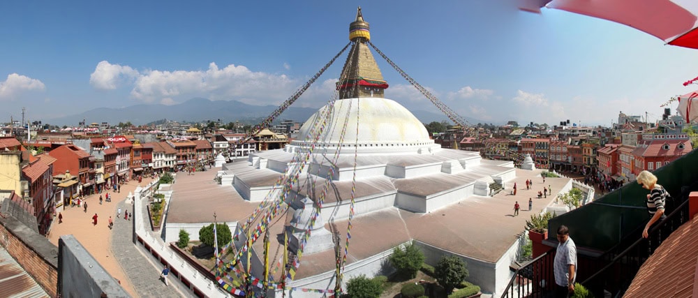 Panoramic view of the Boudhanath Stupa, a white dome with a golden spire, surrounded by buildings and colorful prayer flags in Kathmandu, Nepal—a perfect addition to any family photobook.