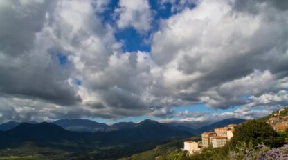 A hillside town under a partly cloudy sky, with a vast green valley and mountain range in the background, is worth a thousand words.