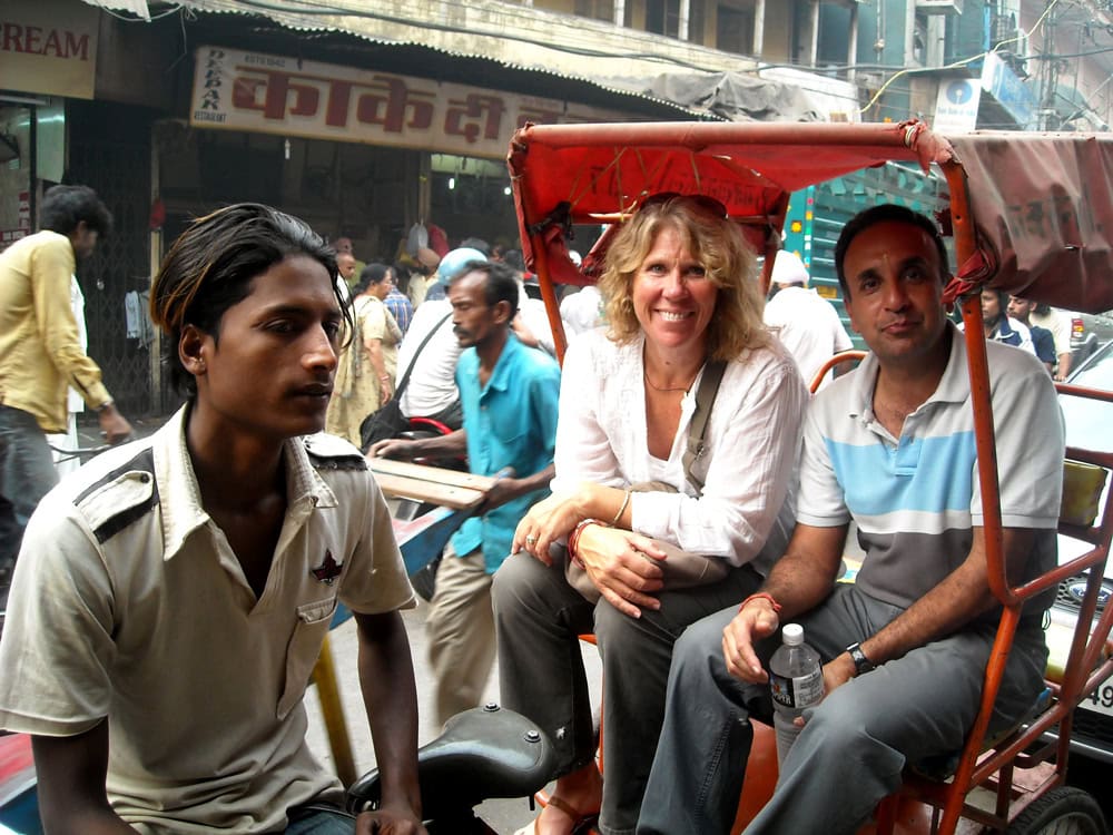 Three people sit on a bicycle rickshaw in a busy street market in Nepal. The rickshaw driver is at the front, and two passengers, a woman and a man, are seated behind him. This scene could be straight out of a family photobook capturing everyday life.