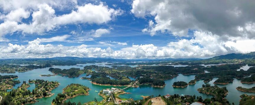 Aerial view of a vast landscape in Colombia, featuring numerous blue lakes, green islands, and scattered buildings under a partly cloudy sky—truly an amazing experience.