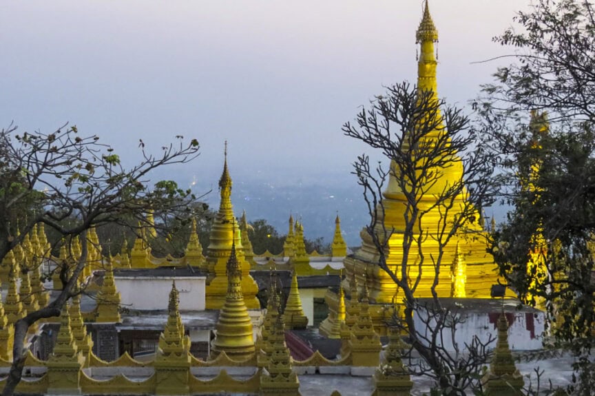 A view of golden pagodas surrounded by trees at dusk in Myanmar, with a hazy sky adding an air of mystery to the scene.