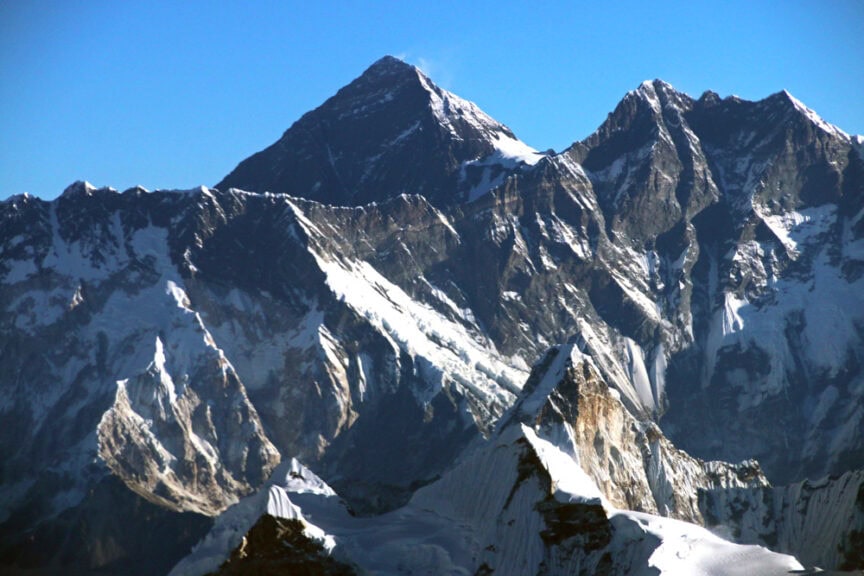 A serene bird's eye view of majestic, snow-covered mountain peaks under a clear blue sky.